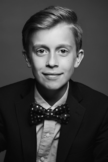 A black-and-white photo of a young boy smiling into the camera, wearing a bowtie. 