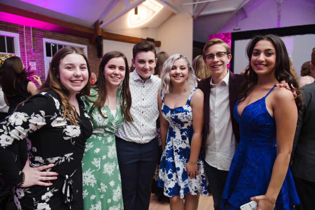 A group of six young people with their arms around each other, smiling into the camera. 